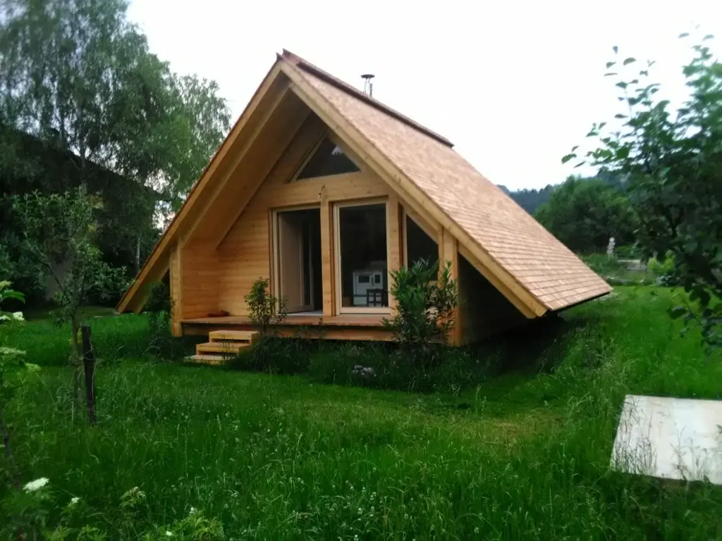 Fertiges Nurdachhaus in Kirchberg mit Holzschindeldach, verglaster Giebelfront, Holzterrasse und Stufen in einer Wiese